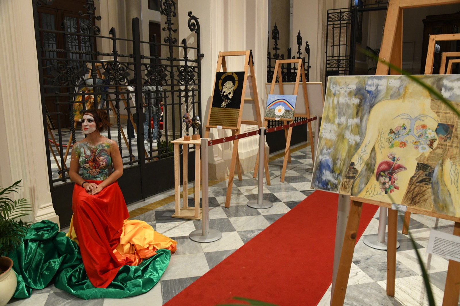 La mostra d'arte del congresso: opere su cavalletti nell'atrio dell'università e una modella dipinta a corpo, seduta accanto a esse