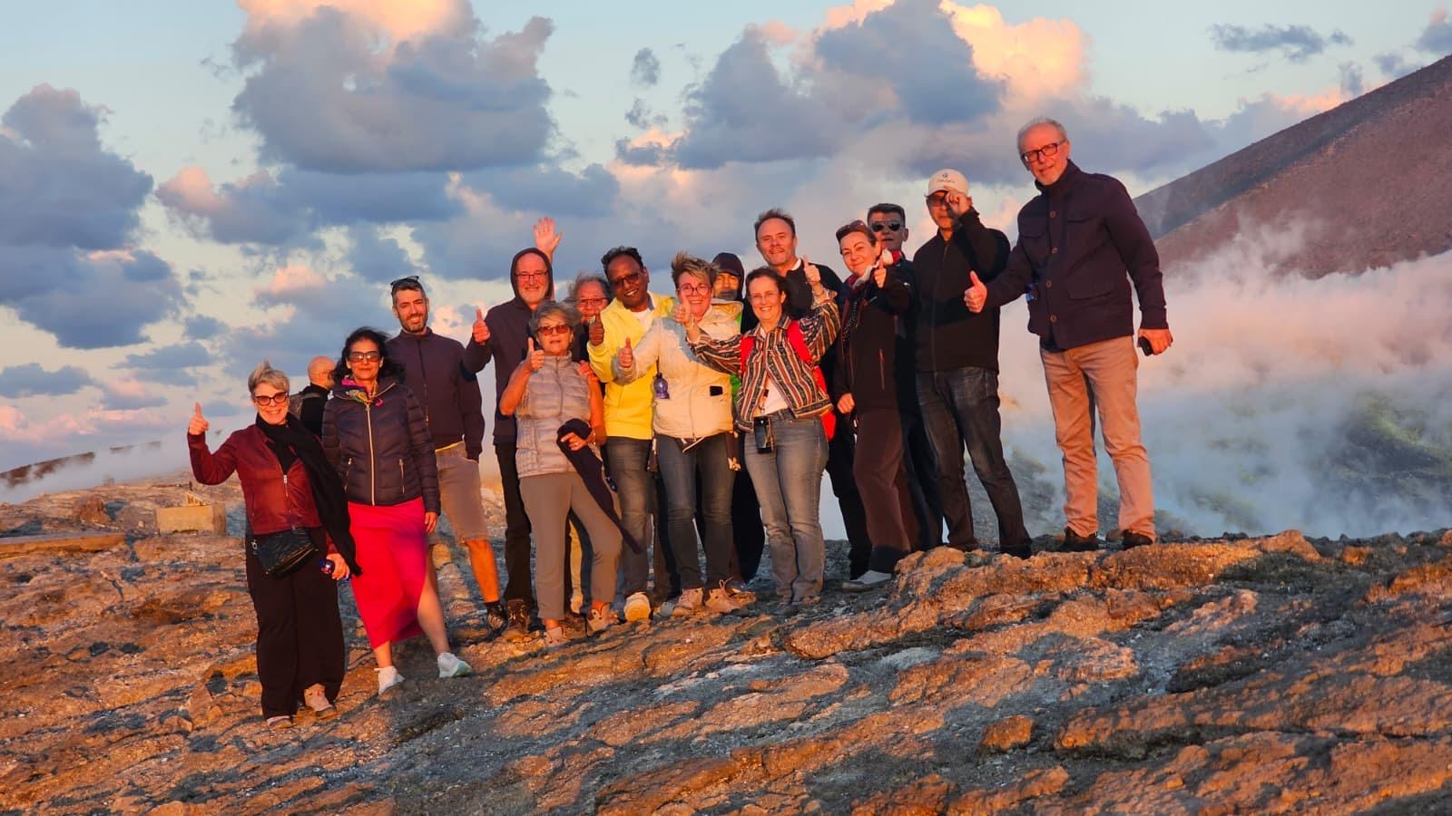 La faculty di DONARTE 2025 sul cratere di Vulcano, nelle Isole Eolie, al tramonto, in piedi sulla roccia con i fumi delle fumarole alle spalle